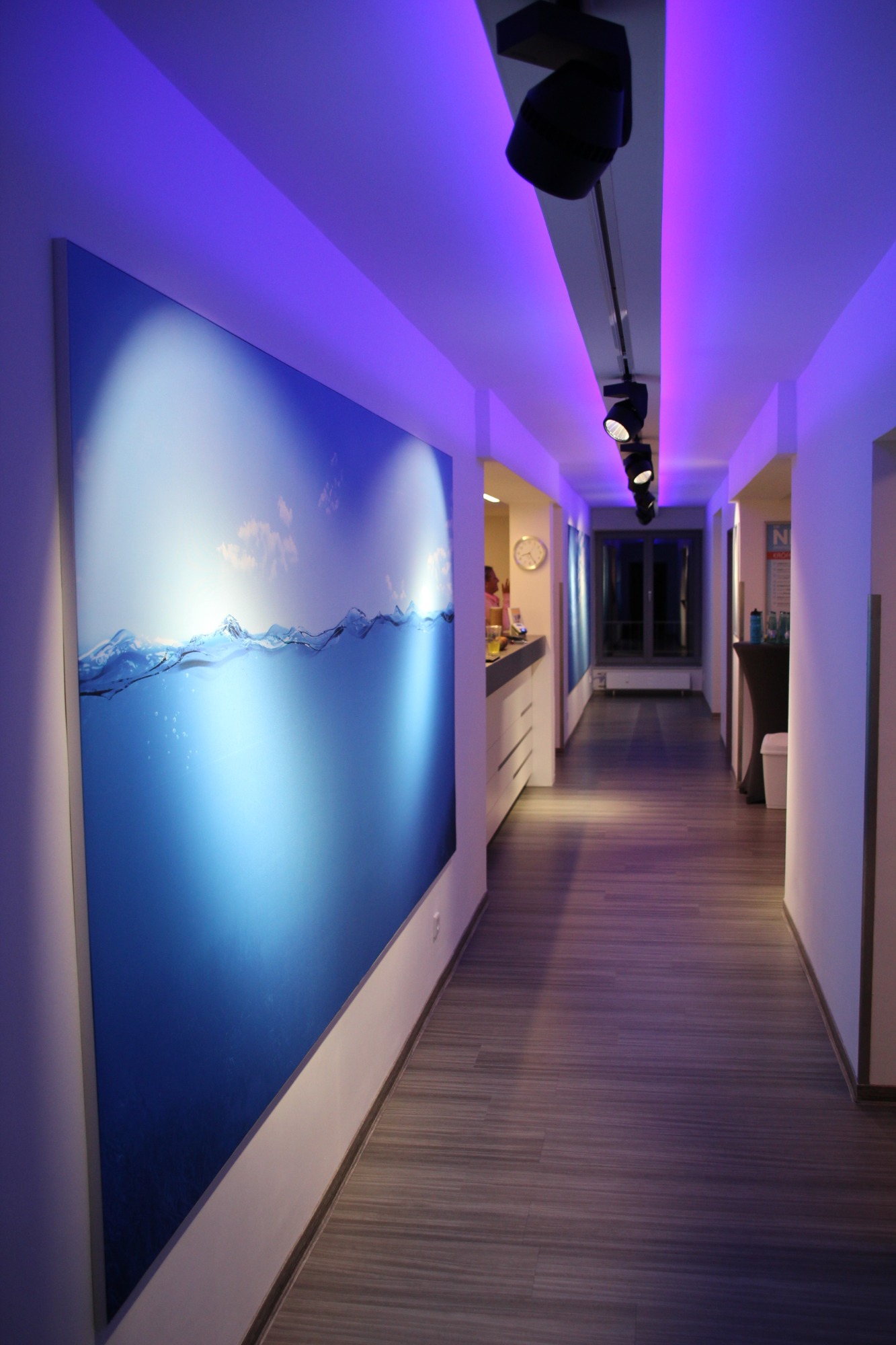 Heller Flur mit blauer Wandmalerei und farbigem Lichtdesign.