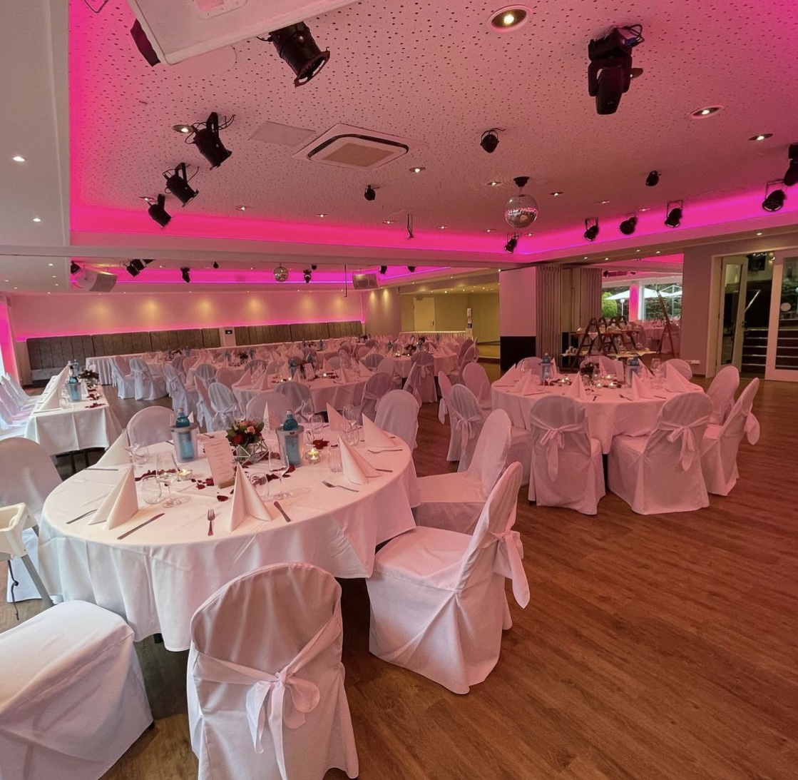Eleganter Veranstaltungsraum mit runden Tischen und pinker Beleuchtung.