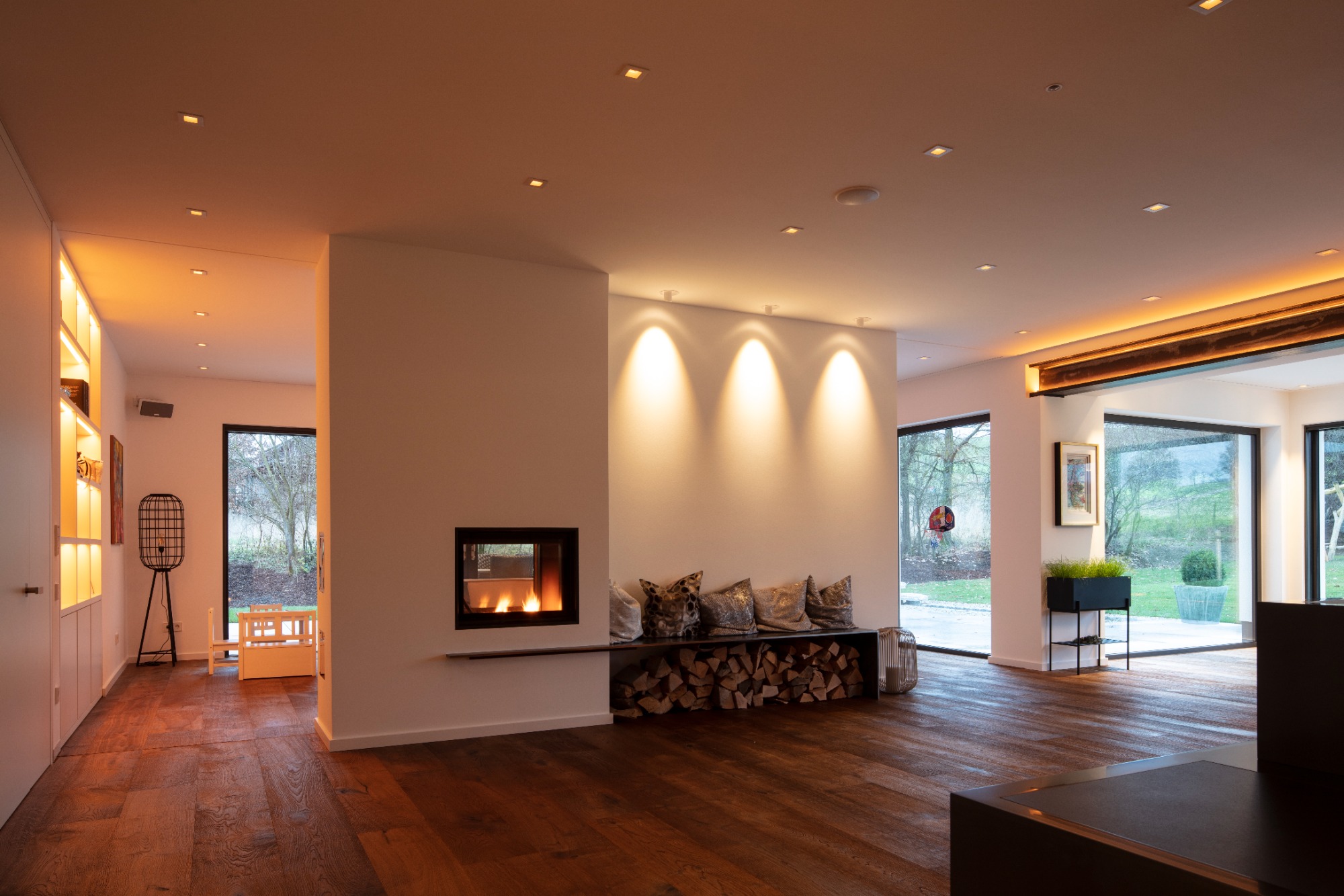 Geräumiges, modernes Wohnzimmer mit Holzfußboden, Kamin und großen Fenstern.