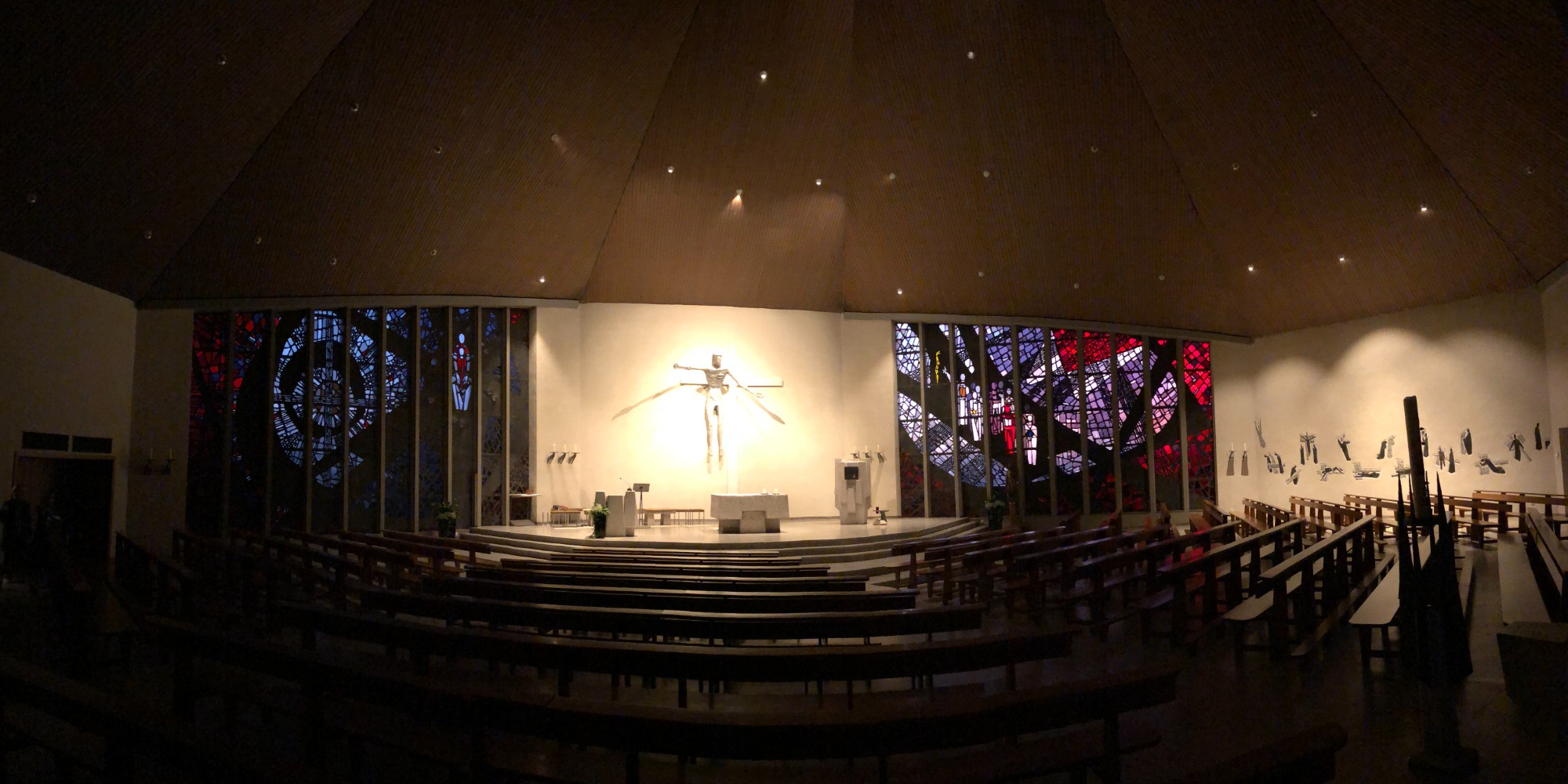 Innenansicht einer Kirche mit bunten Fenstern und einem Altar im Vordergrund.