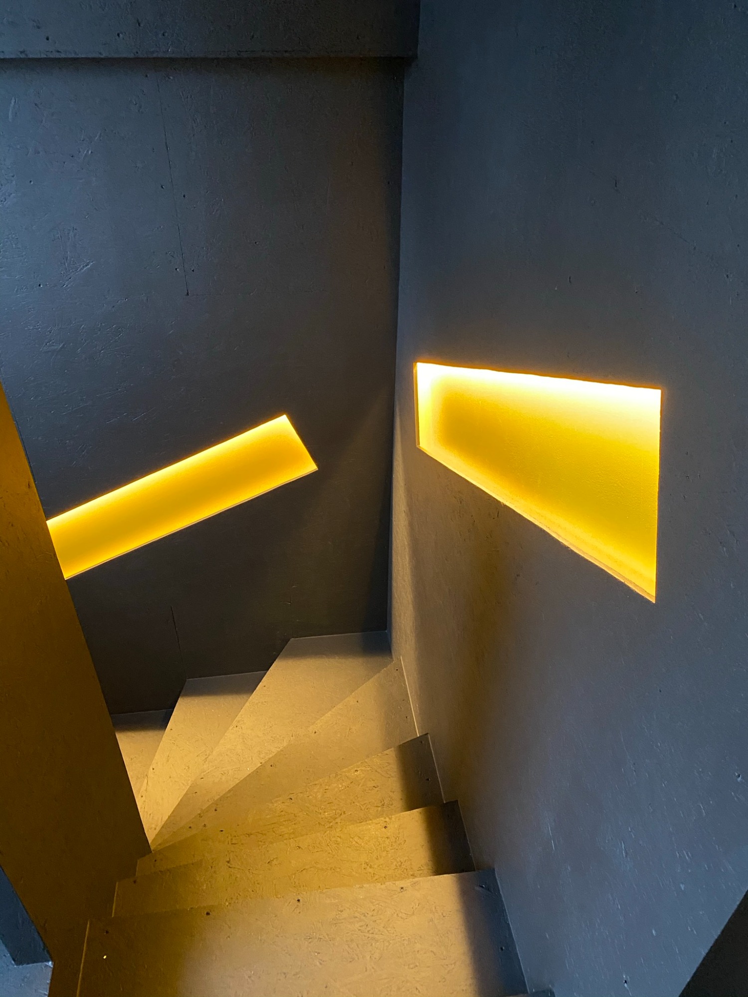 Dunkler Treppenaufgang mit warmem, schmalem Lichtakzent an der Wand.