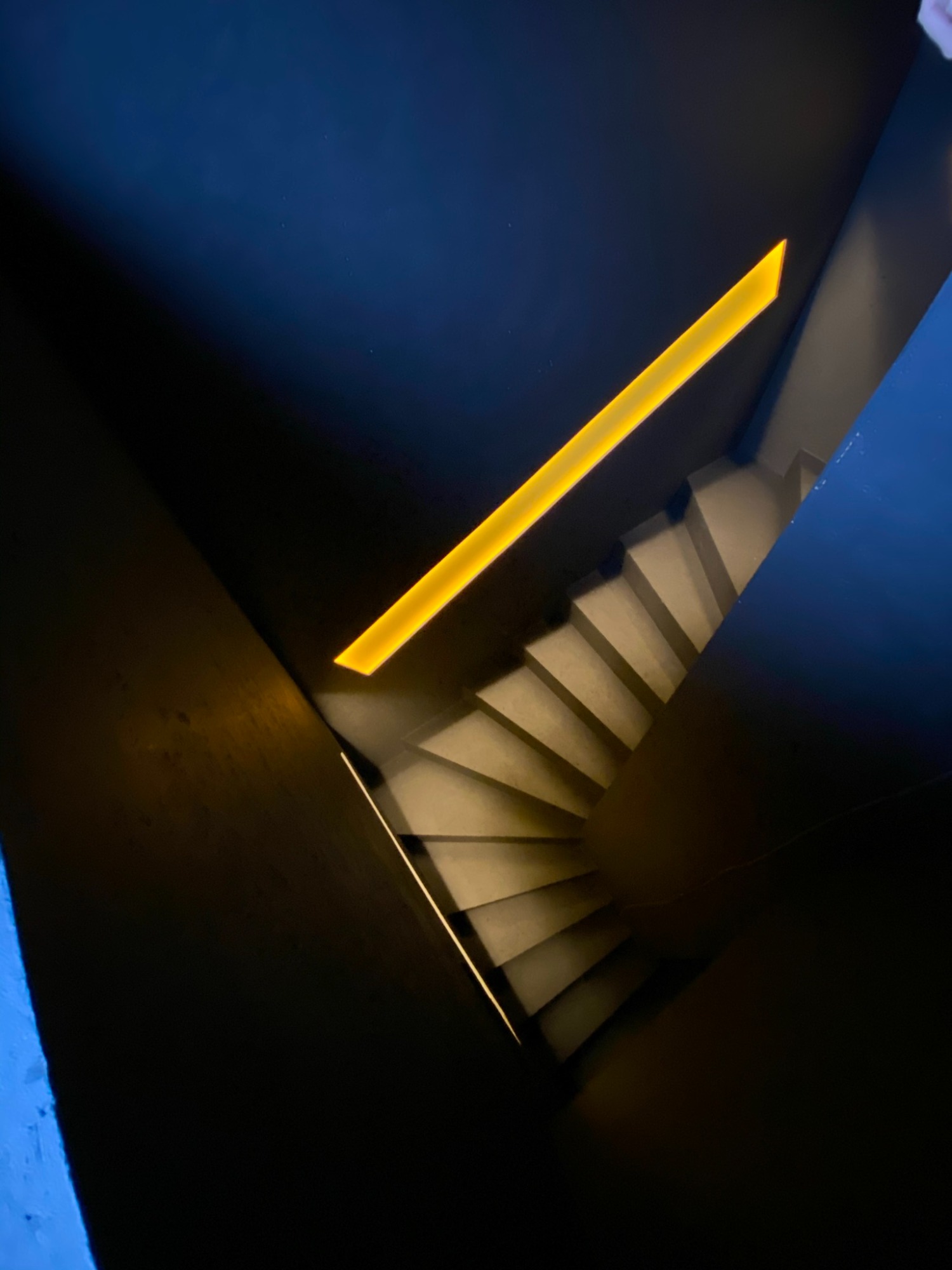 Schwarze Treppe mit sanftem Licht und gelbem Lichtstreifen oben.